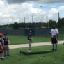 Group of campers watching coach give instruction to pitcher on mound