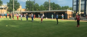 Two lines of campers warm up with stretches in grassy outfield at Columbus State
