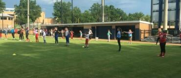 Two lines of campers warm up with stretches in grassy outfield at Columbus State