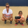 Coach Jamie Wohlbach squats alongside three campers in catcher position