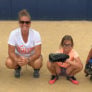 Coach Jamie Wohlbach squats alongside three campers in catcher position
