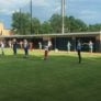 Two lines of campers warm up with stretches in grassy outfield at Columbus State