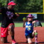 Young girl mirrors throwing motion of softball coach while on one knee